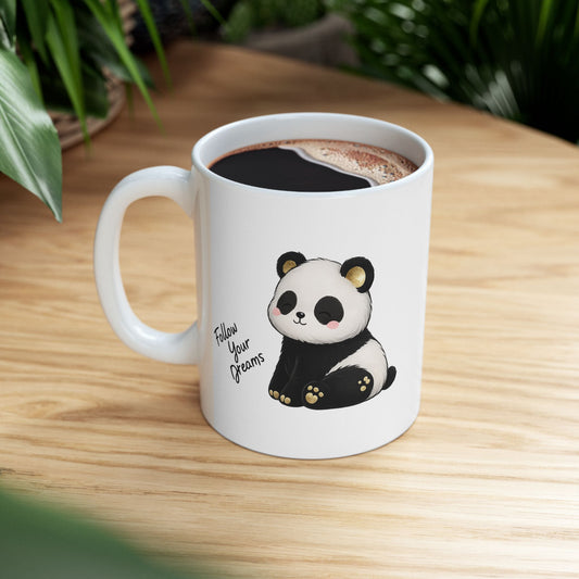 White mug with a panda design and 'Follow Your Dreams' text on a wooden table.